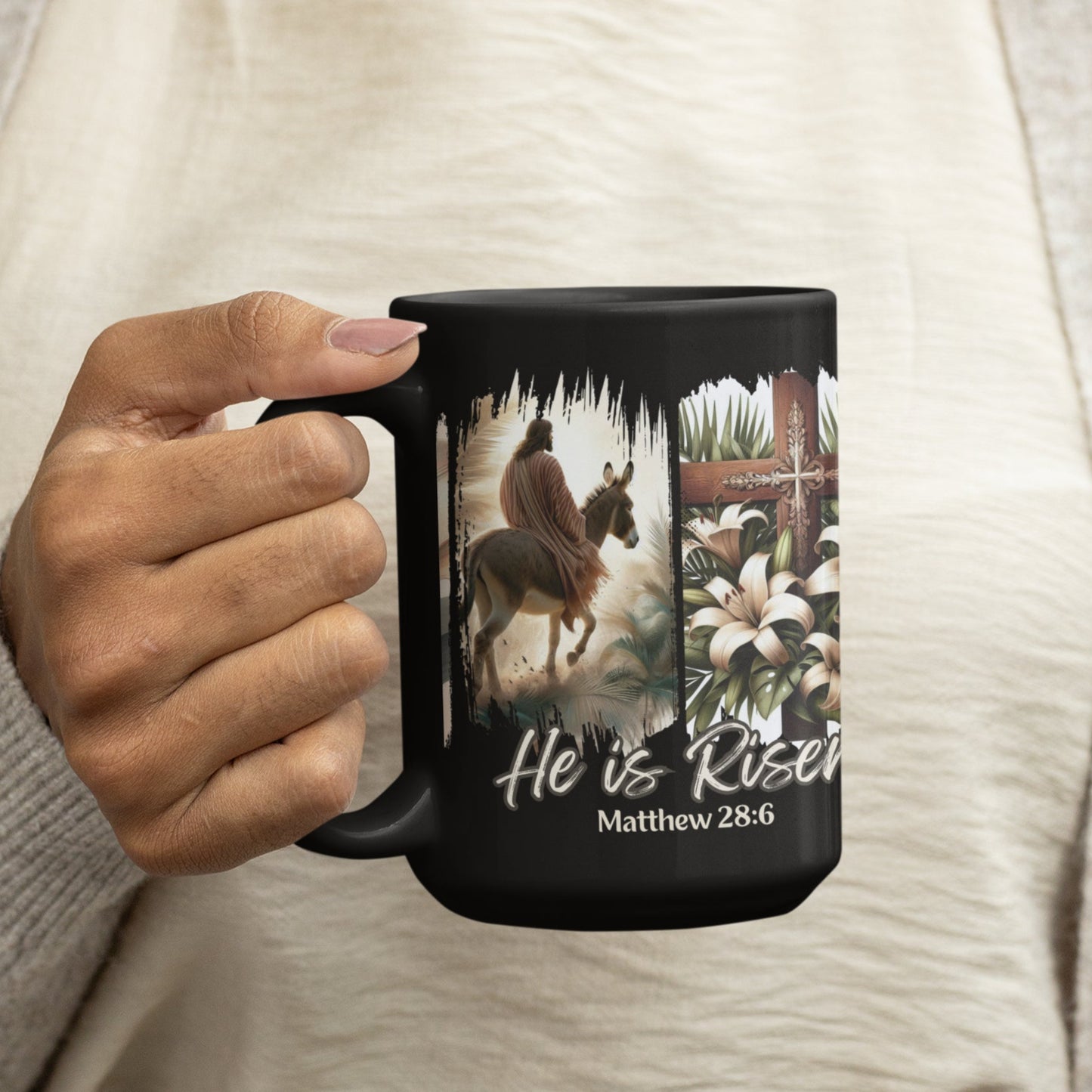 Black 15oz coffee mug with a depiction of Jesus riding a donkey, a detailed cross adorned with lilies, and elegant floral touches, all set against a dramatic black brushstroke backdrop. Also features the words He is Risen! and the Bible verse Matthew 28:6 at the bottom of the mug.