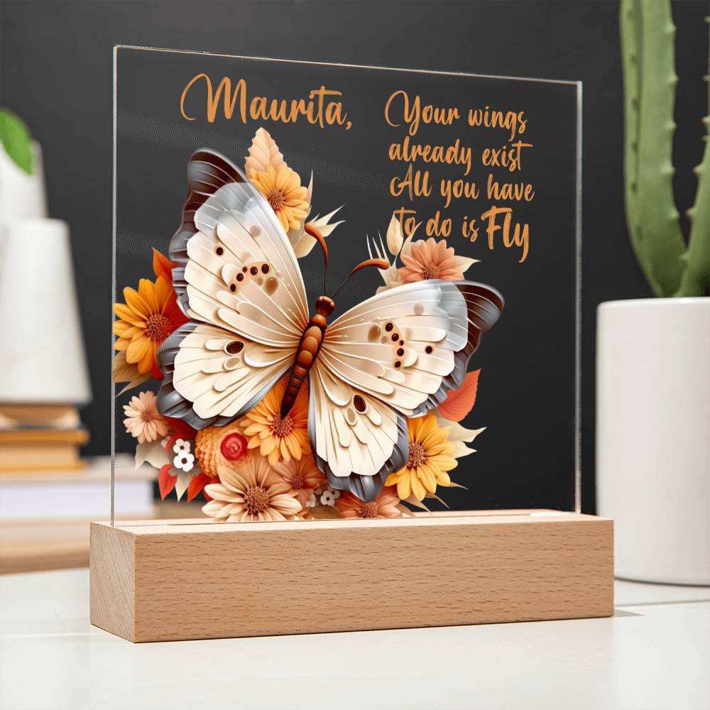 A clear acrylic plaque with LED base has a 3D butterfly in the colors of tan, beige and gray. Butterfly is surrounded by orange, yellow, peach, and tan flowers. Plaque sits in a light brown wooden base. Has a place to personalize name along with a message of encouragement. That reads "Your wings already exist All you have to do is fly."