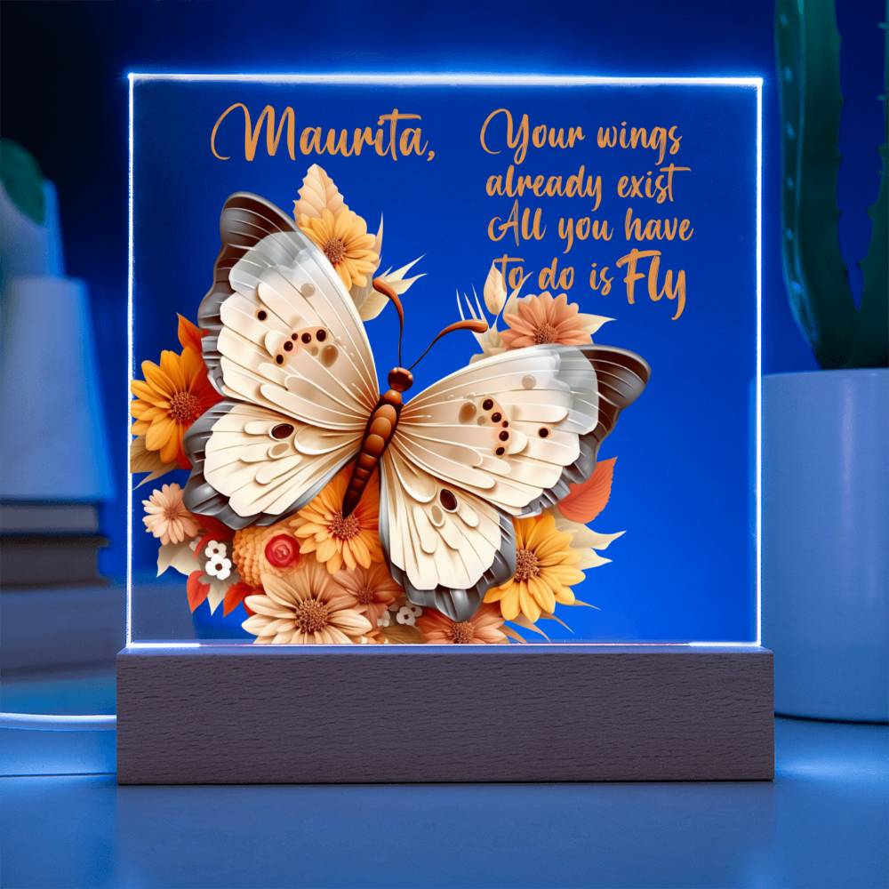A clear acrylic plaque with blue LED light shining on a 3D butterfly in the colors of tan, beige and gray. Butterfly is surrounded by orange, yellow, peach, and tan flowers. The wooden base is light brown. Has a place to personalize name along with a message of encouragement. That reads "Your wings already exist All you have to do is fly."