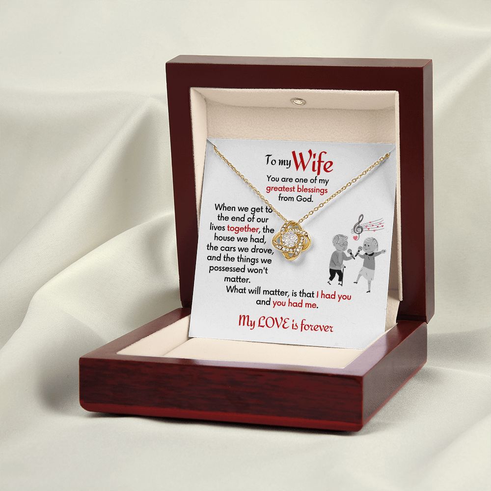 To Wife 18k yellow gold finish Love Knot necklace with jewelry message card. Card features special message to wife with an elderly man and woman singing together. Card is white background. In a mahogany box with card standing inside.