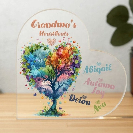 Clear acrylic heart shaped plaque features an image of a watercolor tree with hearts as leaves. Colors of pink, blue, green, orange and teal hearts. Plaque reads Nana's Heartbeats and includes personalization of grandkids names in the color of the tree.