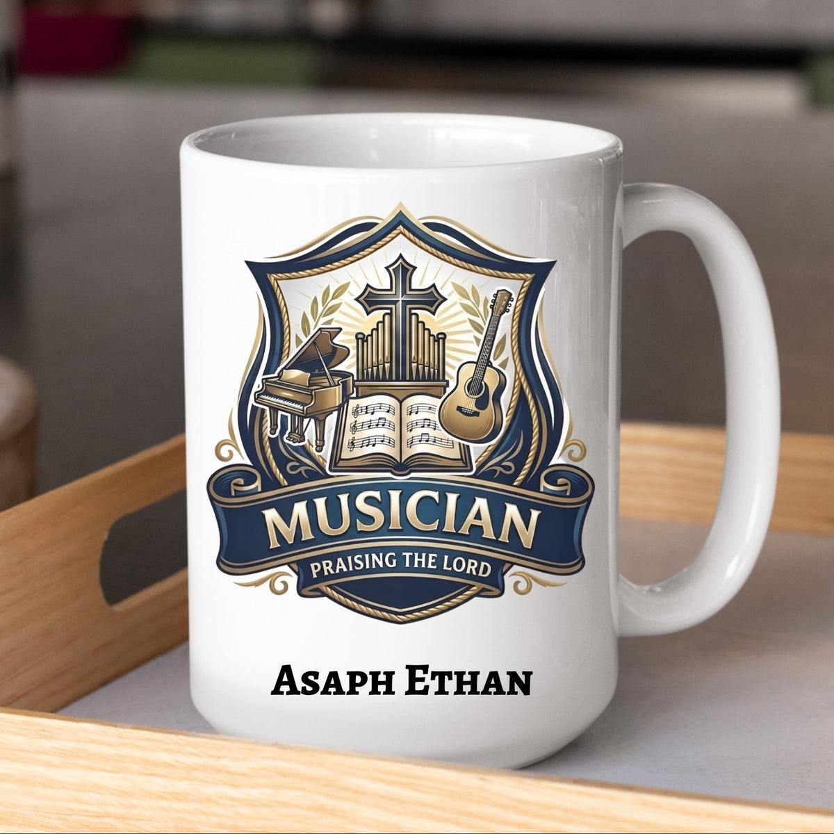 A white ceramic coffee mug with a custom printed crest design for a musician, featuring a cross, piano, guitar, and an open song book, with the text 'MUSICIAN PRAISING THE LORD' and the personalized name 'Asaph Ethan' printed below. The mug is sitting on a light wooden tray in a blurred kitchen setting.