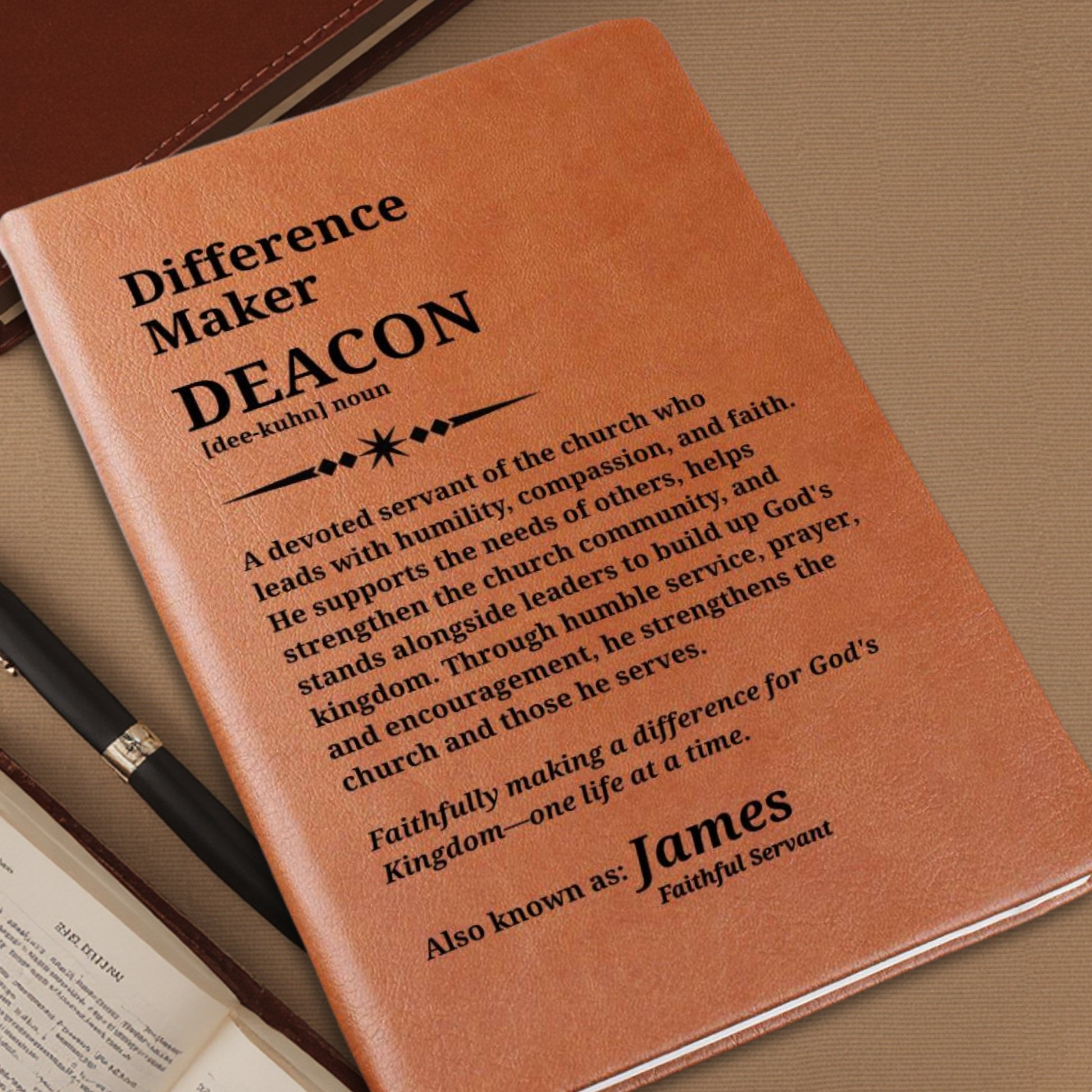 A close-up of a tan leather-bound book or journal cover with black printed text reading 'Difference Maker DEACON' and a definition, photographed on a brown textured surface with part of a pen and an open book visible.