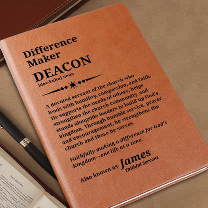 A close-up of a tan leather-bound book or journal cover with black printed text reading 'Difference Maker DEACON' and a definition, photographed on a brown textured surface with part of a pen and an open book visible.