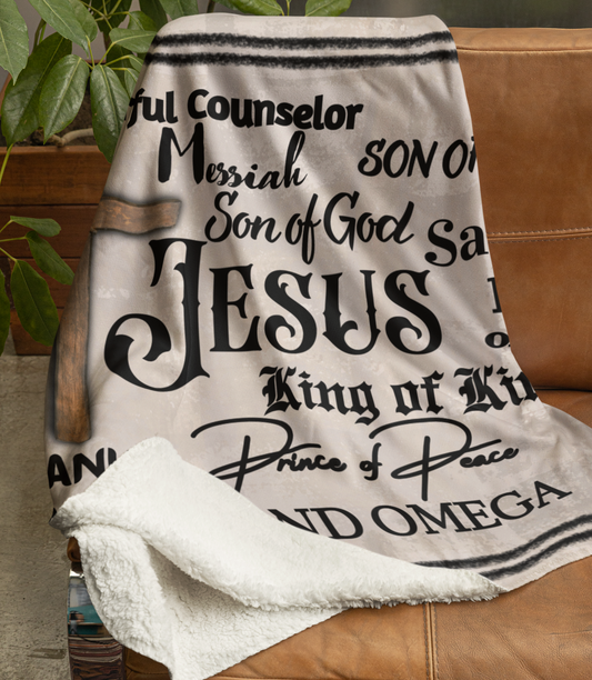 The Names of Jesus Throw Blanket is tan with black text throughout the blanket. It features a brown cross and the names of Jesus in different font types. Some names included are: Prince of Peace, King of Kings, Messiah, and so forth.
