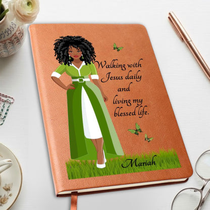 A personalized brown notebook with a textured cover, featuring an illustration of a Black woman in a green and white dress with the quote 'Walking with Jesus daily and living my blessed life.' and the name 'Mariah' at the bottom.