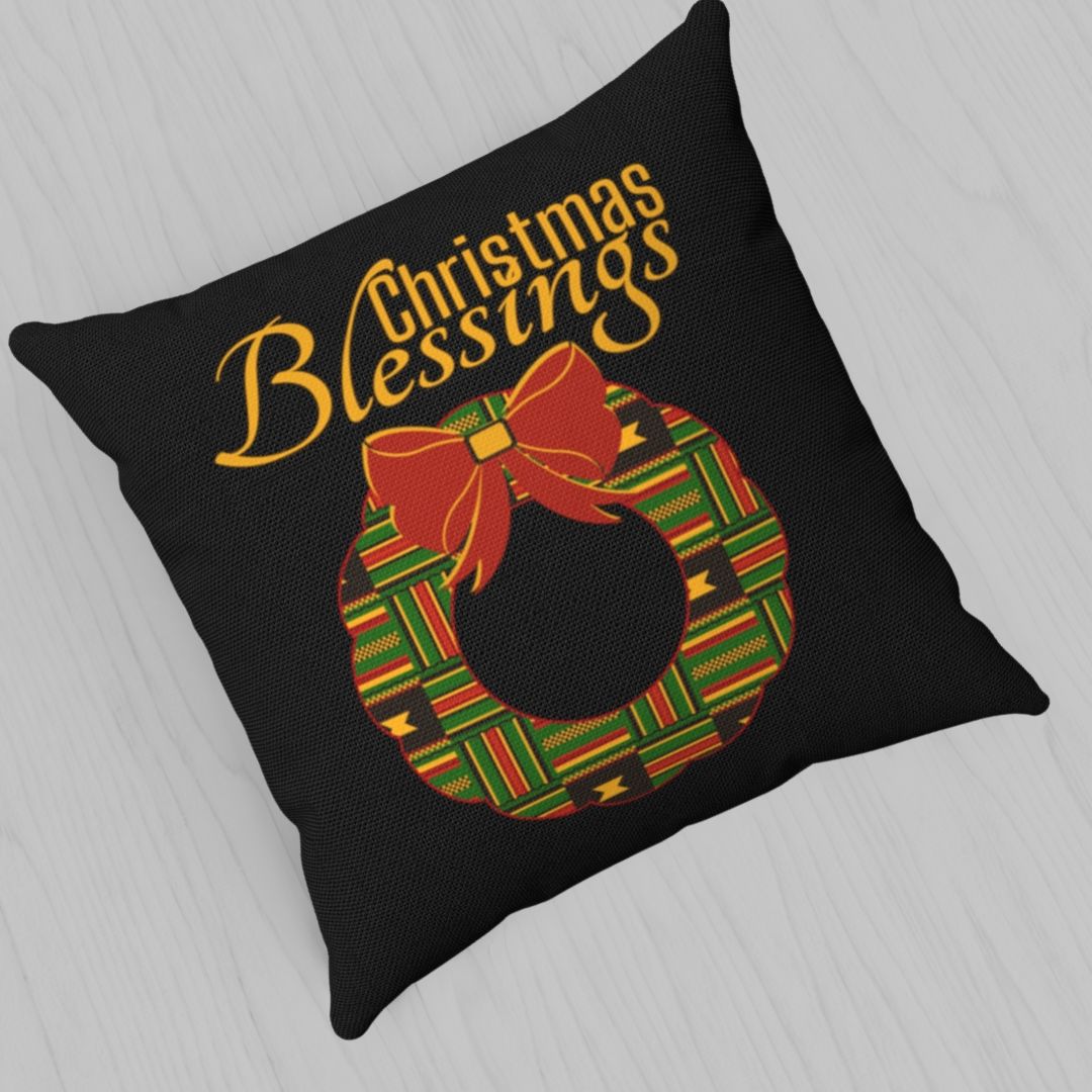 Black pillow with Kente pattern Christmas wreath, and red bow. The words Christmas Blessings is above the wreath.