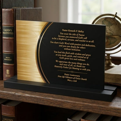 Pastor appreciation plaque with printed gold text on a matte background, sitting on a black acrylic stand with books and a globe in the background.