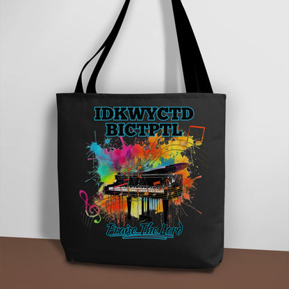 A black tote bag with a bright and colorful piano design and the text KWYCTDBICTPTL - Praise the Lord.