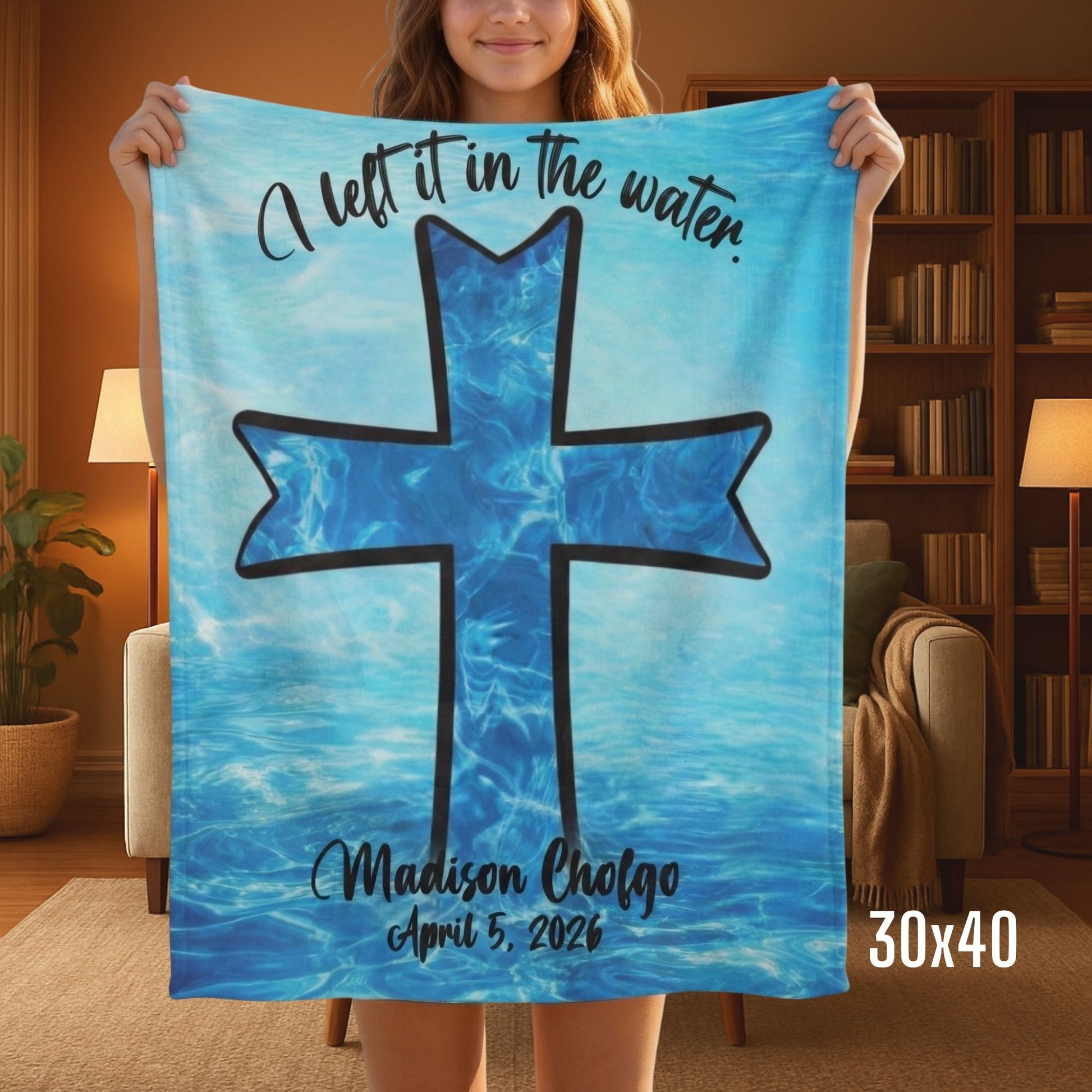 A person standing in a living room holding a small blue Sherpa baptism blanket that has an image of a cross in the water.