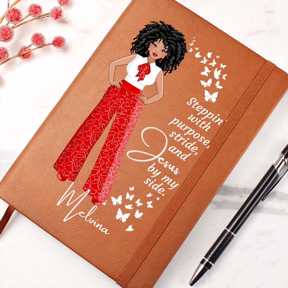 African American female dressed in red and white pants and shirt on front cover of a vegan leather writing journal. Quote on journal reads: "Steppin' with purpose, stride and Jesus by my side." in a white font. Also has white butterflies on the front cover and bookmark.