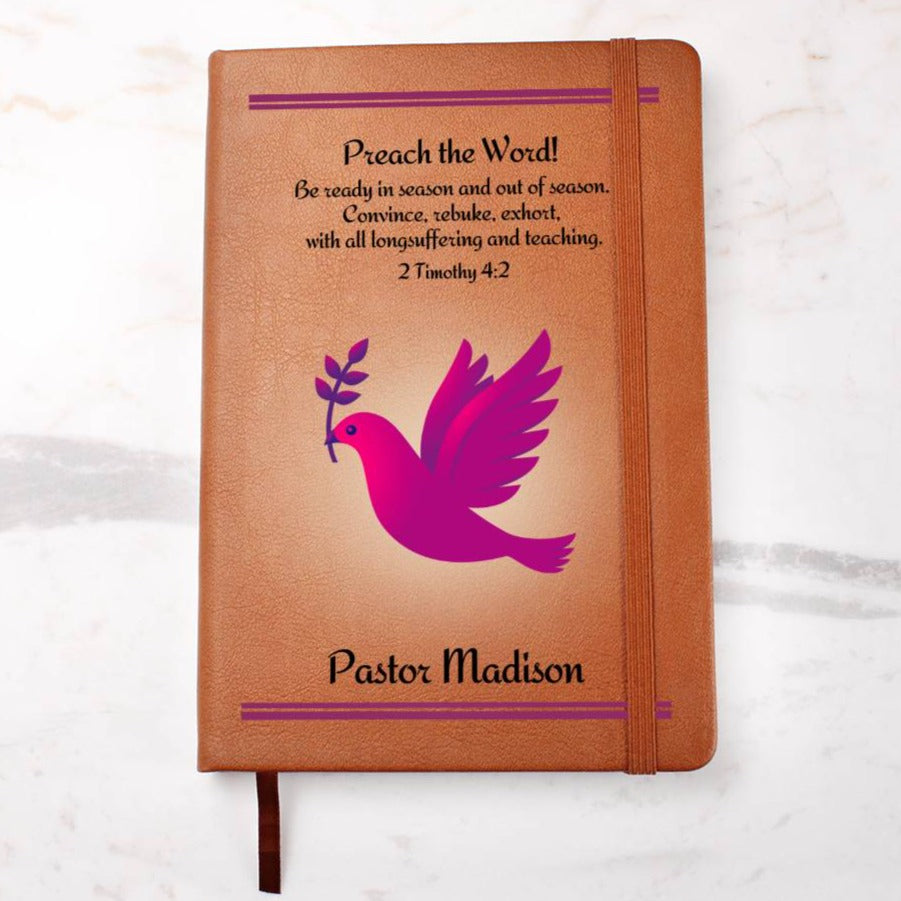 A leather writing journal for a female pastor.  The brown vegan journal features on it's cover a fuchsia dove with a twig in it's beak and the Bible verse 2 Timothy 4:2. The words Preach The Word as well as the personalized name of the minister is in bold letters.