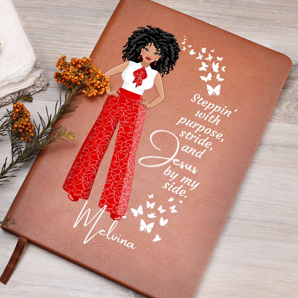 African American female dressed in red and white pants and shirt on front cover of a vegan leather writing journal. Quote on journal reads:  "Steppin' with purpose, stride and Jesus by my side." in a white font. Also has white butterflies on  the front cover.