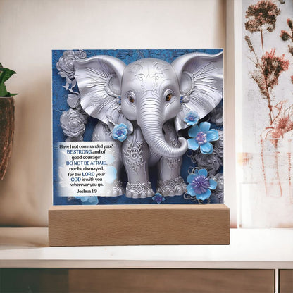 3D print of elephant and flowers on an acrylic plaque that sits on a wooden base. Elephant is in front a beautiful blue background and also features Bible verse Joshua 1:9.
