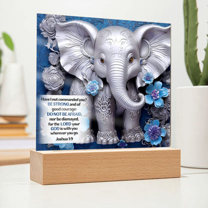 Image of a silver 3D elephant print with 3D flowers on an acrylic plaque that sits on a wooden base. Elephant is in front a beautiful blue swirled background and also features Bible verse Joshua 1:9.