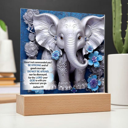 Image of a 3D silver elephant and flowers on an acrylic plaque that sits on a wooden base. Elephant is in front a beautiful blue background and also features Bible verse Joshua 1:9.