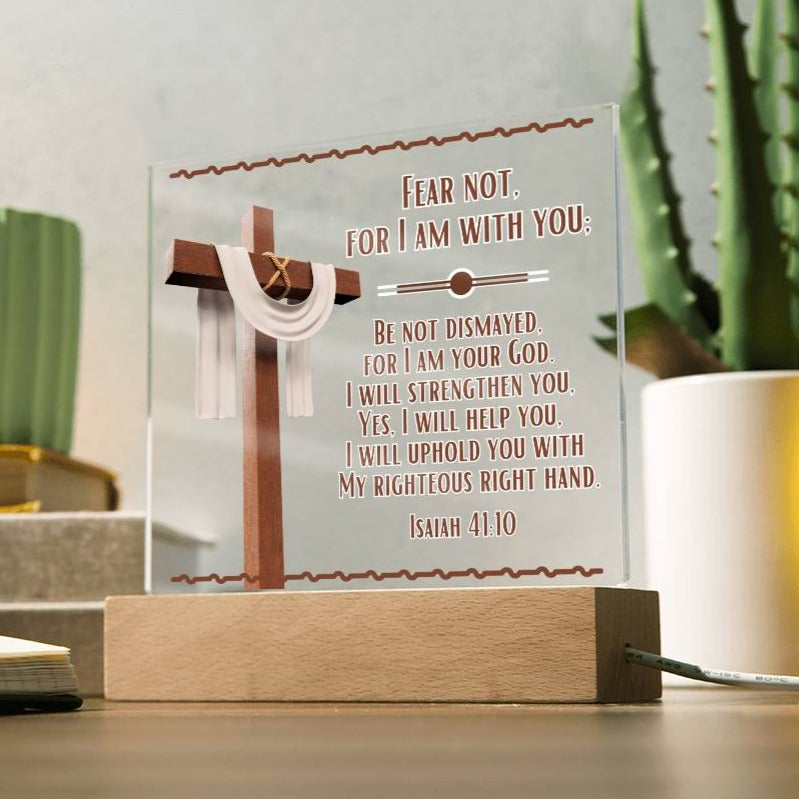 Image is of a clear acrylic square plaque and features Bible verse Isaiah 41:10.  Fear Not For I Am With You...  Also  has a 3d image of a brown cross with a beige scarf draped over it. The acrylic square sits in a wooden base.