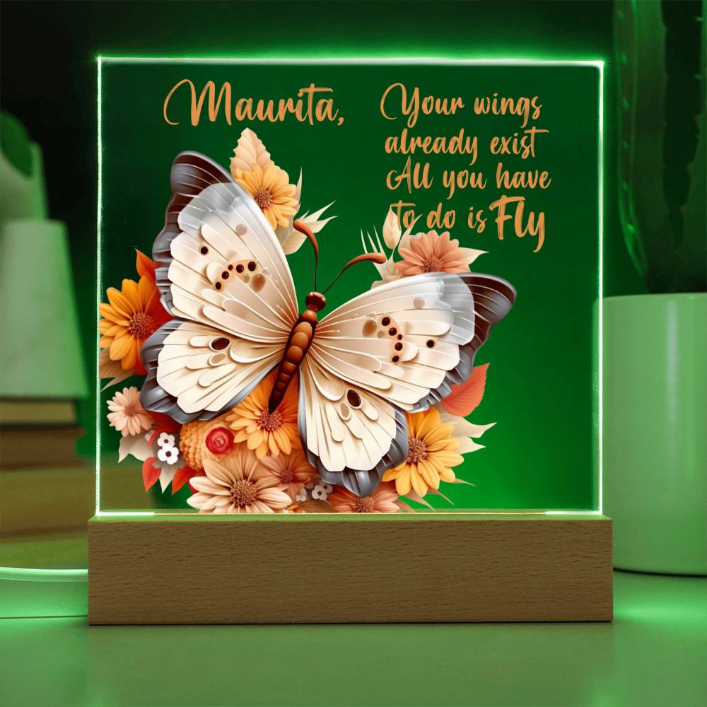 A clear acrylic plaque shown with a green LED light on a 3D butterfly in the colors of tan, beige and gray.  Butterfly is surrounded by orange, yellow, peach, and tan flowers. Plaque sits in a light brown wooden base. Has a place to personalize name along with a message of encouragement. That reads "Your wings already exist All you have to do is fly." 
