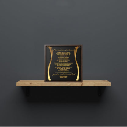 Framed pastor appreciation plaque with gold text on a wooden shelf against a dark gray wall.