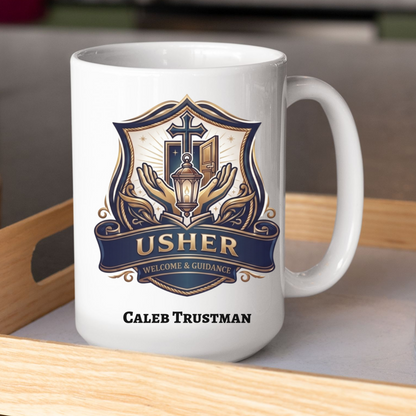 A white ceramic coffee mug with a custom printed crest design in navy blue, gold, and beige, featuring the text 'USHER' and 'WELCOME & GUIDANCE' with the personalized name 'CALEB TRUSTMAN' printed below. The mug is sitting on a light wood tray next to a clear glass tumbler.