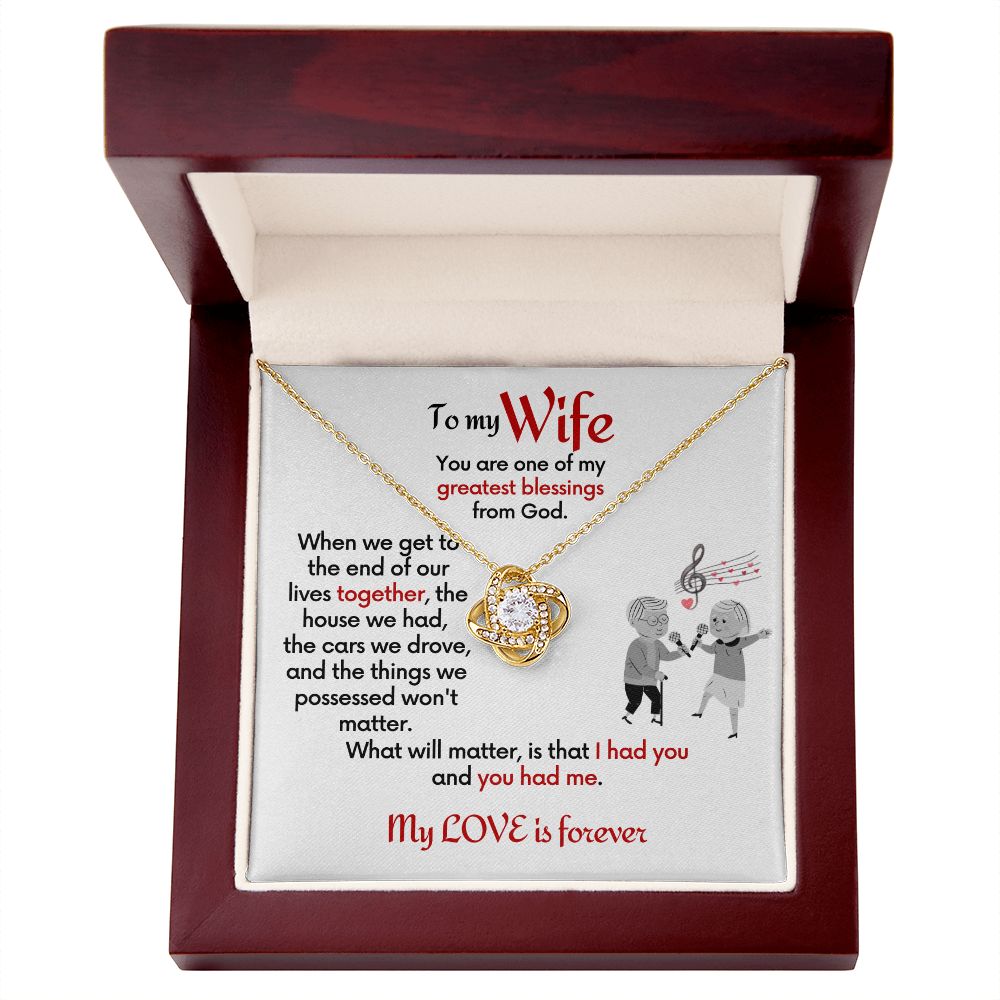 To Wife 18k yellow gold finish Love Knot necklace with jewelry message card. Card features special message to wife with an elderly man and woman singing together. Card is white background. In a mahogany box.