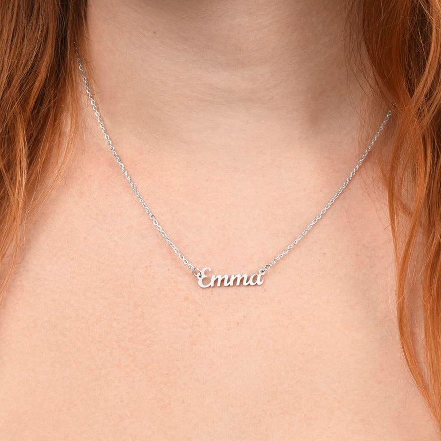 American Stainless Steel custom name necklace being warn by a red head young lady. Close up of models neck reveals the name "Emma." Name featured here is 'Imani." Supports up to 8 characters for the name necklace. Name height measures 0.3".